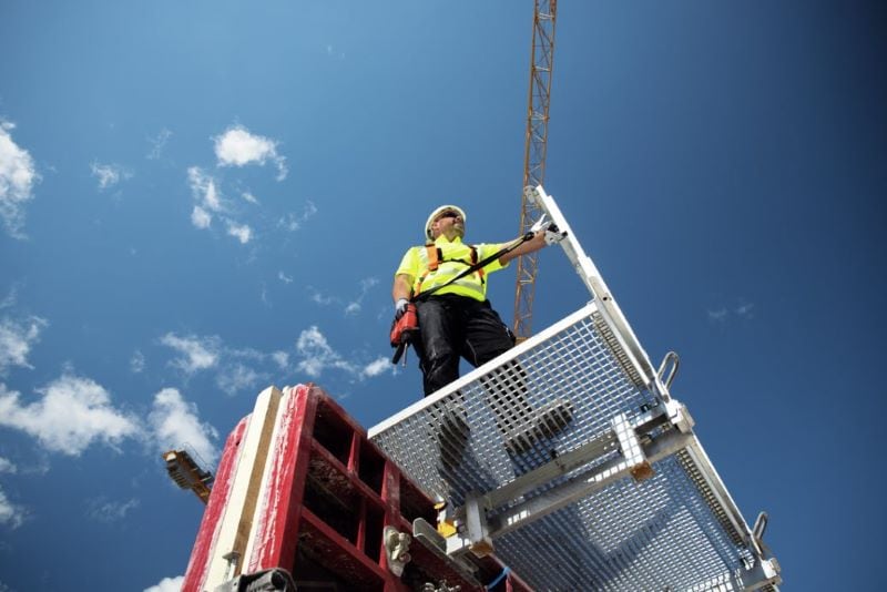 Worker standing on a platform with a drill in his hand that is fixed to a pole with a tool tether