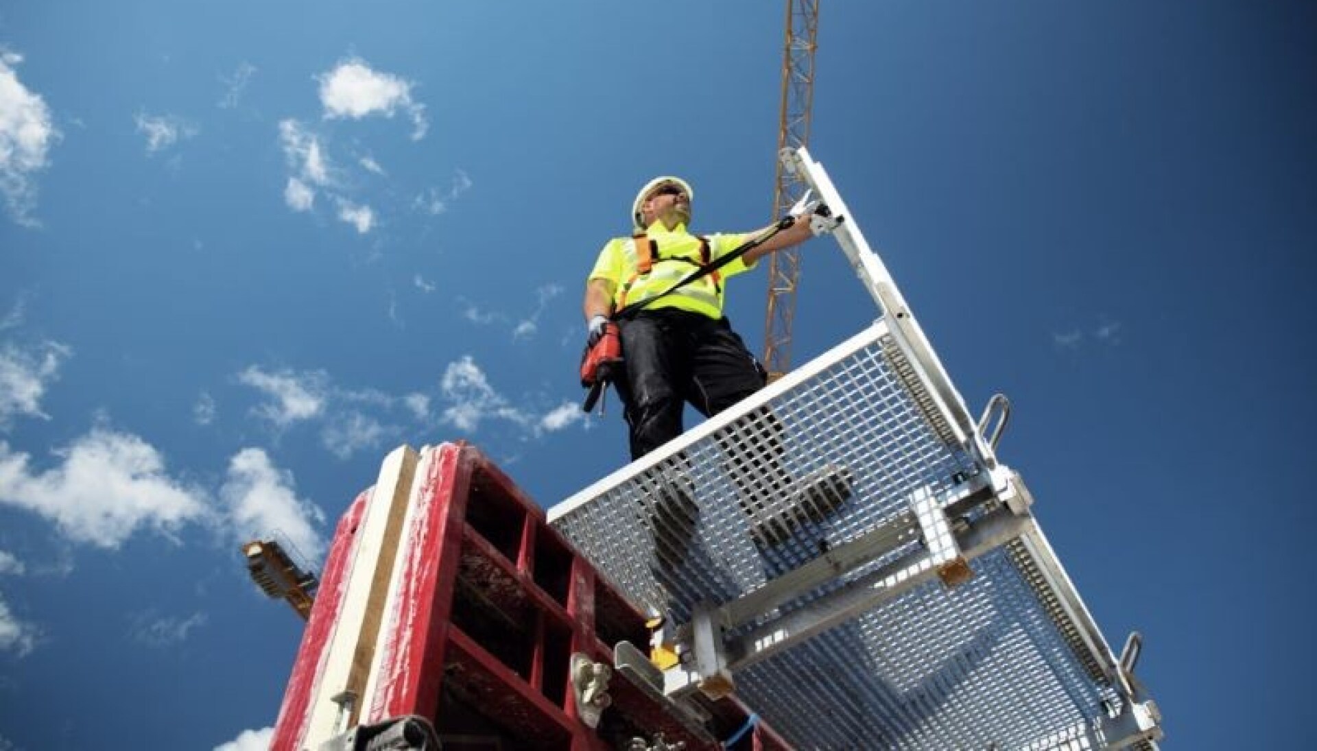 Worker standing on a platform with a drill in his hand that is fixed to a pole with a tool tether